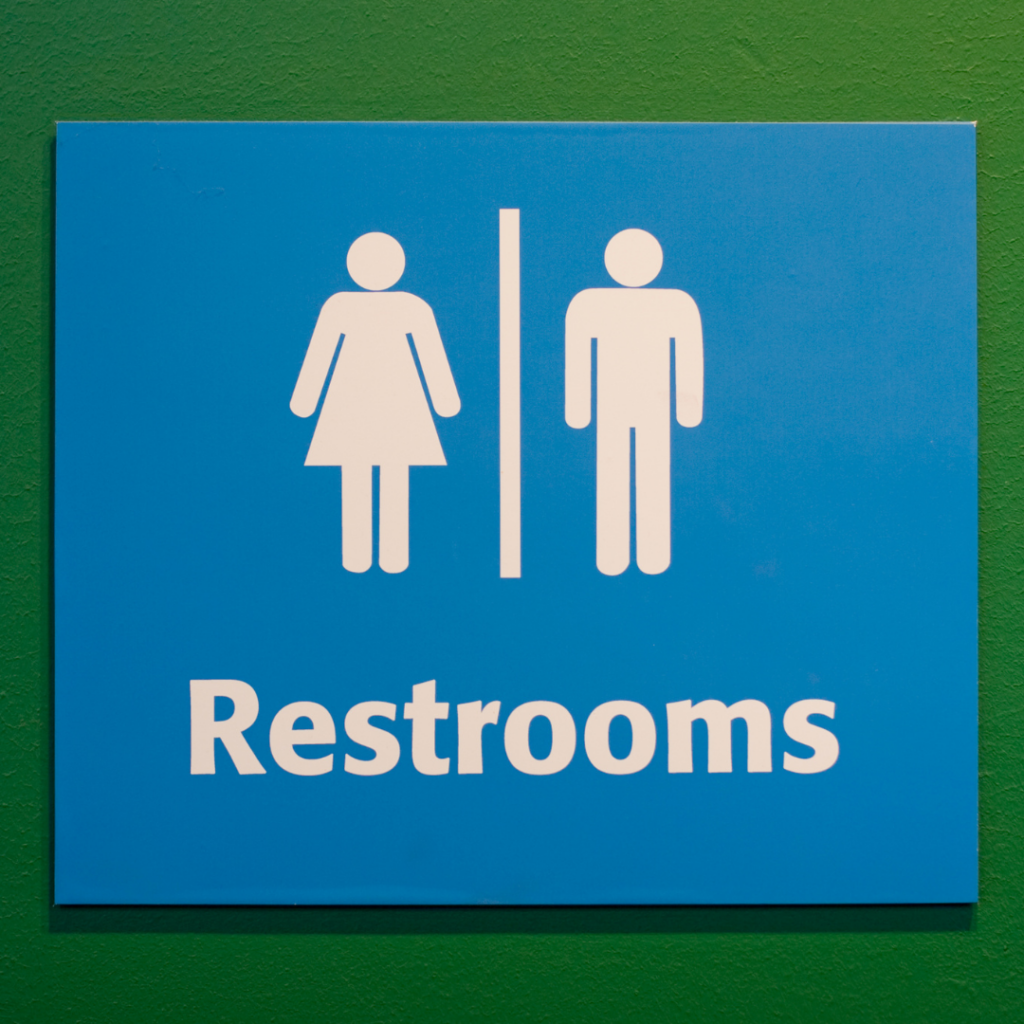 Blue restroom sign with male and female icons on a green wall.