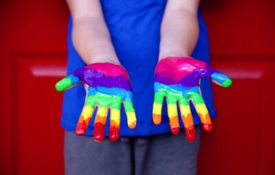 Person holding out hands painted with rainbow colors against a red background.