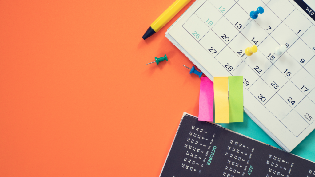 Calendar, colorful sticky notes, pen, and pushpins on an orange background.