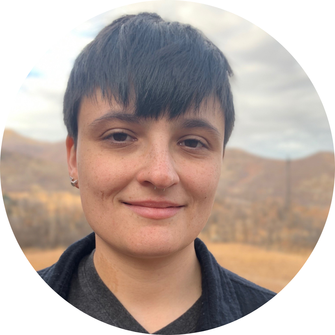 Person with short dark hair smiling outdoors in a mountainous area.