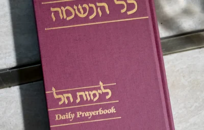 A maroon daily prayer book with gold embossed Hebrew and English text on a marble surface.