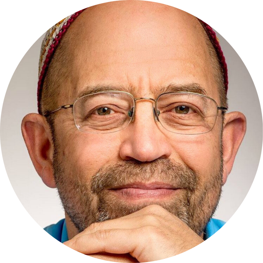 Man with glasses and a patterned cap, resting his chin on his hand, smiling at the camera.