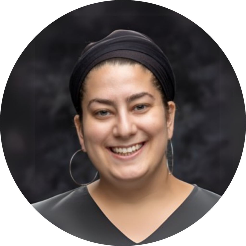 Smiling person wearing a black headwrap and hoop earrings against a dark blurred background.