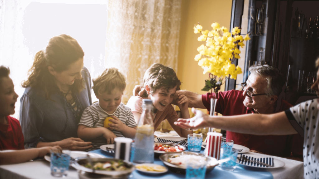 Grandparents and grandchildren eating and laughing around a table with food