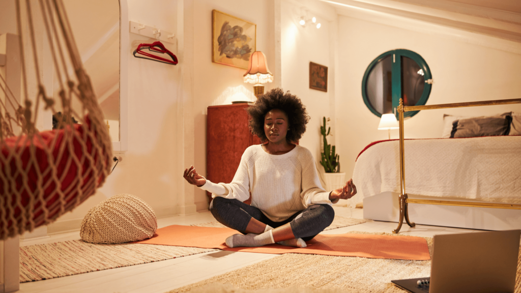 A Black woman meditating inside a white bedroom