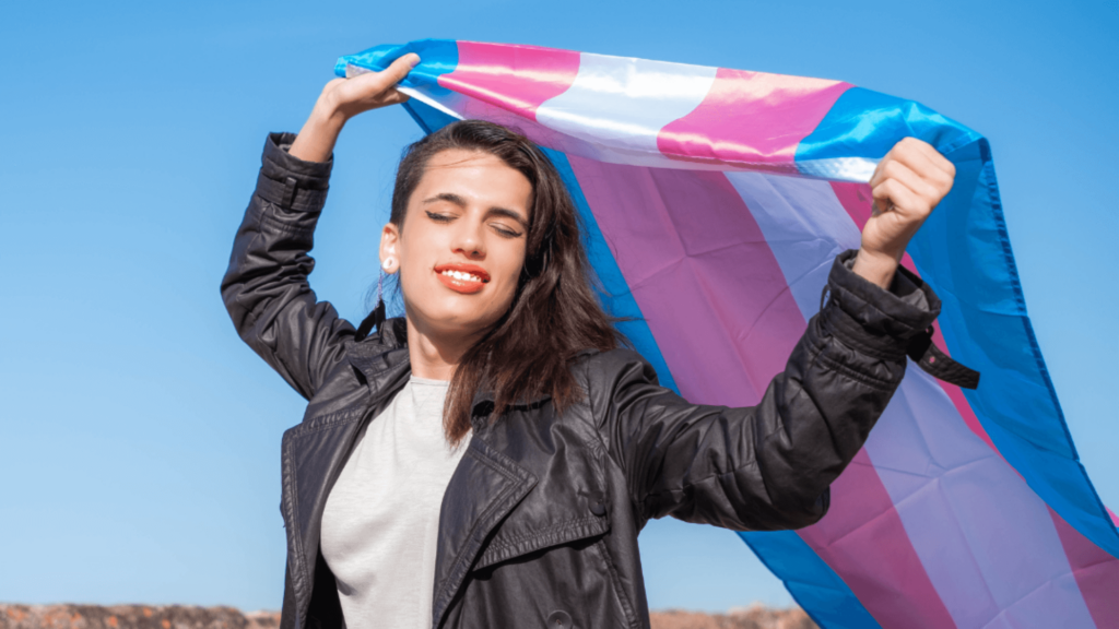 A person with long dark hair holding a trans flag
