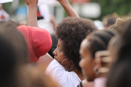 Person in a crowd holding a sign during a protest, wearing a white shirt and hoop earrings.