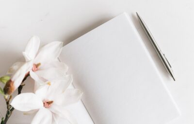 Open notebook with a silver pen and white flowers on a white surface.