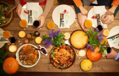 Table set for Thanksgiving with roast chicken, pies, drinks, and fall decorations. Four people seated around it.