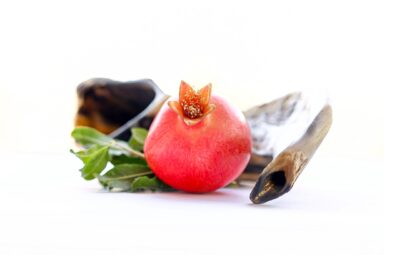 Pomegranate and shofar on a white background with green leaves.