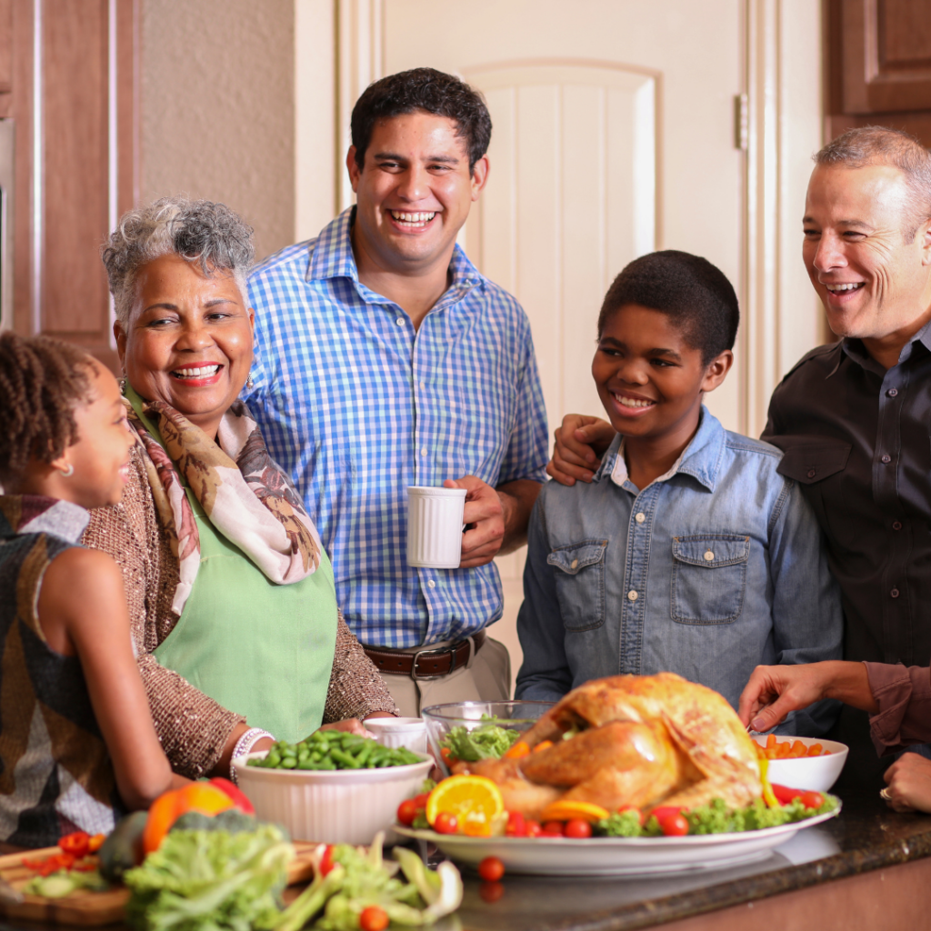 A family smiling and gathered in the kitchen around a table with a turkey and vegetables.