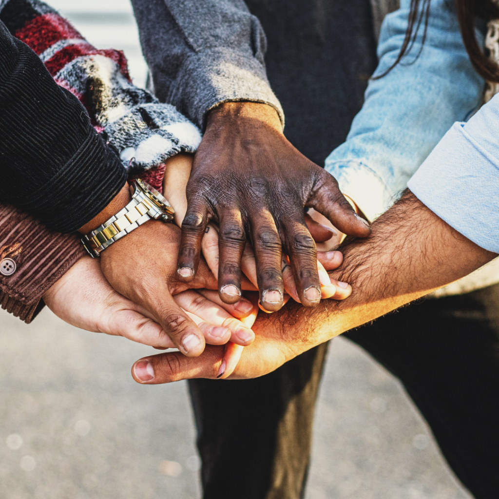 Diverse hands stacked together in a show of unity and teamwork outdoors.