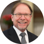 Man with glasses and a beard smiling in a suit and tie.