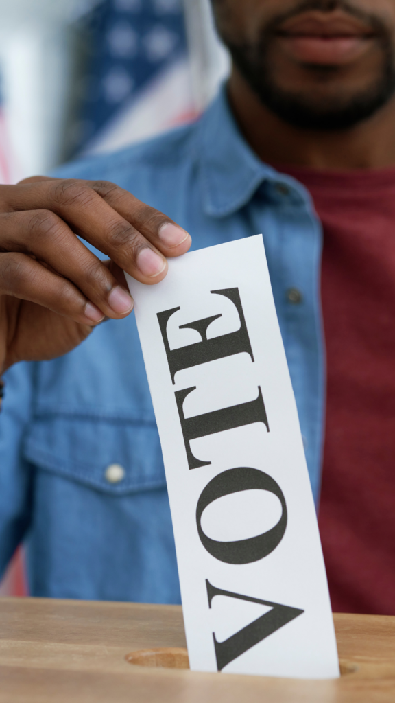A person places a sheet with the word VOTE into a ballot box.