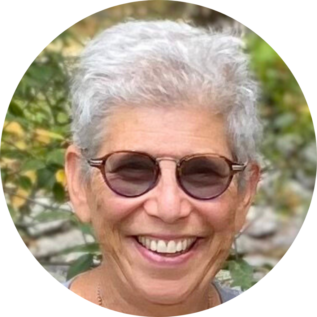 A person with short gray hair and sunglasses smiling outdoors.