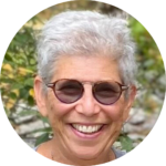 A person with short gray hair and sunglasses smiling outdoors.