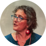 A person with short gray hair, glasses, and red earrings, speaking.