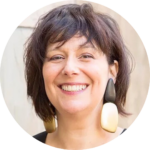 Smiling person with short dark hair and large geometric earrings.