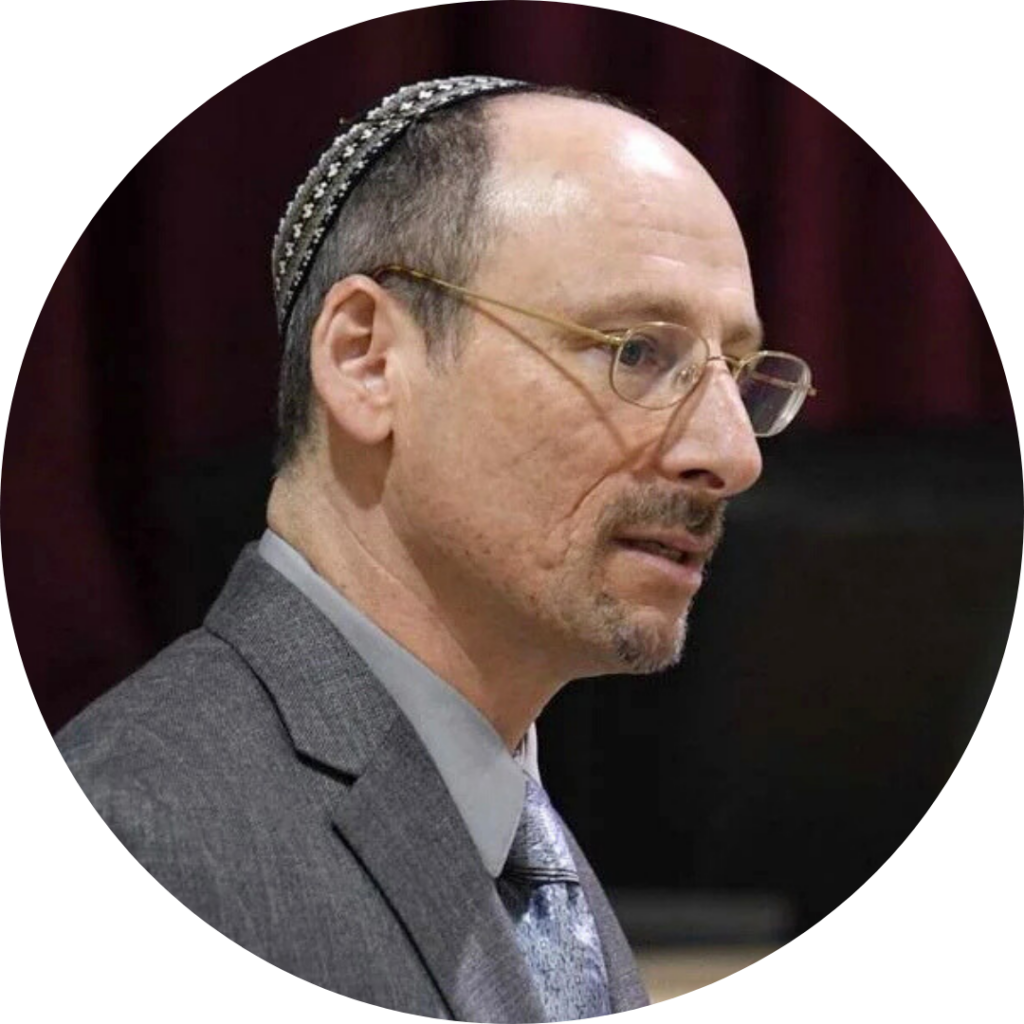 Man wearing glasses and a kippah, dressed in a suit, speaking at an event.
