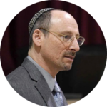 Man wearing glasses and a kippah, dressed in a suit, speaking at an event.