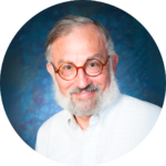A man with glasses and a white beard smiles against a blue background.