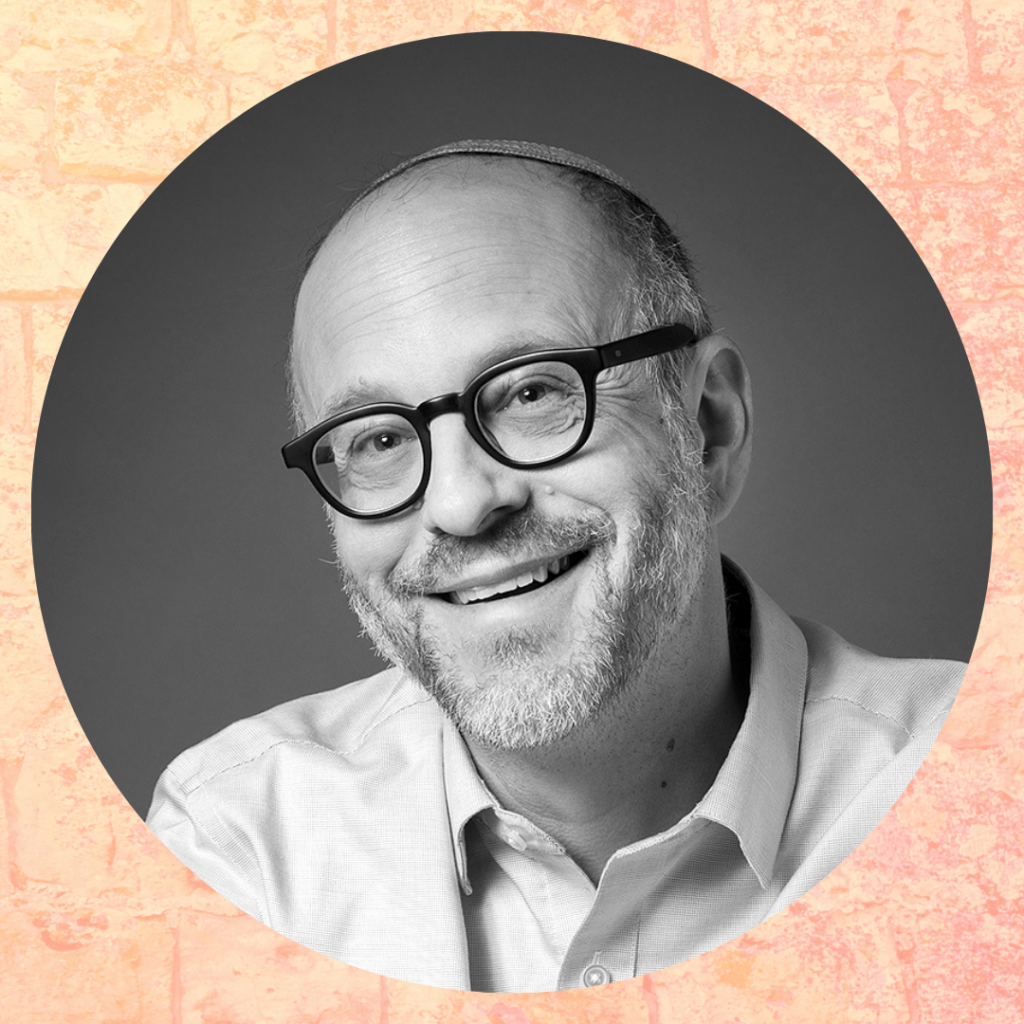 Smiling man with glasses and a beard, wearing a light shirt, on a textured peach background.