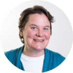 Smiling person with short hair, wearing a teal cardigan and white shirt, against a plain background.