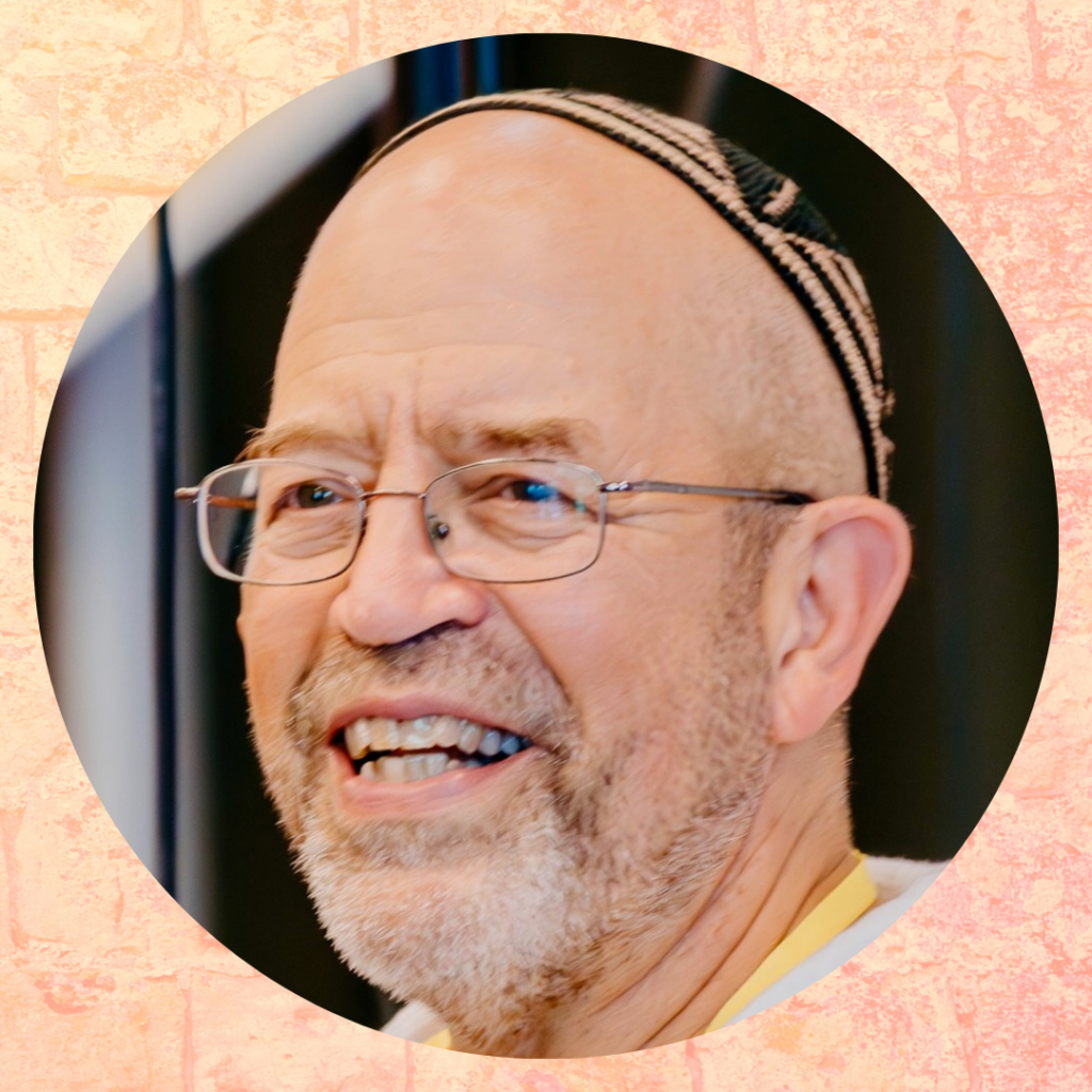 A bearded man with glasses and a kippah is smiling against a textured background.