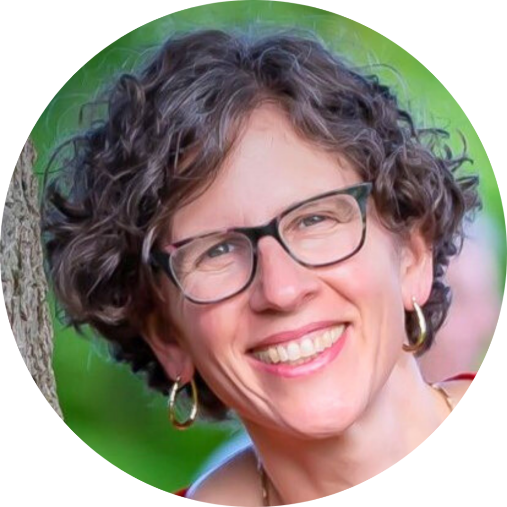 Smiling person with curly hair and glasses, outdoors with greenery in the background.
