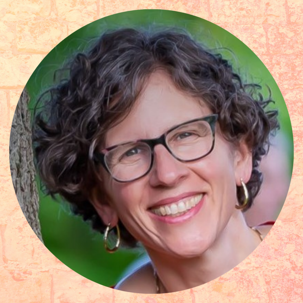 Smiling person with curly hair and glasses against a leafy background.