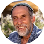 Smiling man wearing a cap in a sunny outdoor setting.
