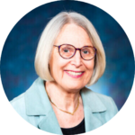 Rabbi Nancy Fuchs Kreimer wearing a turquoise blazer smiles against a blue background.