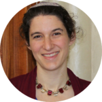 A person with a kippah, smiling warmly, wearing a necklace and a burgundy top.