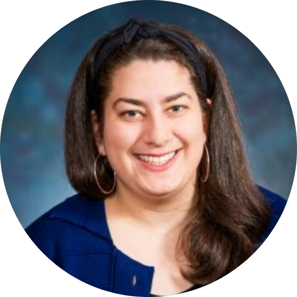 Rabbi Sarah Brammer-Shlay wearing a blue top and hoop earrings, against a blue background.