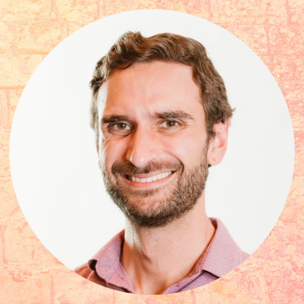 Smiling man with a beard and pink shirt against a white background in a circular frame.
