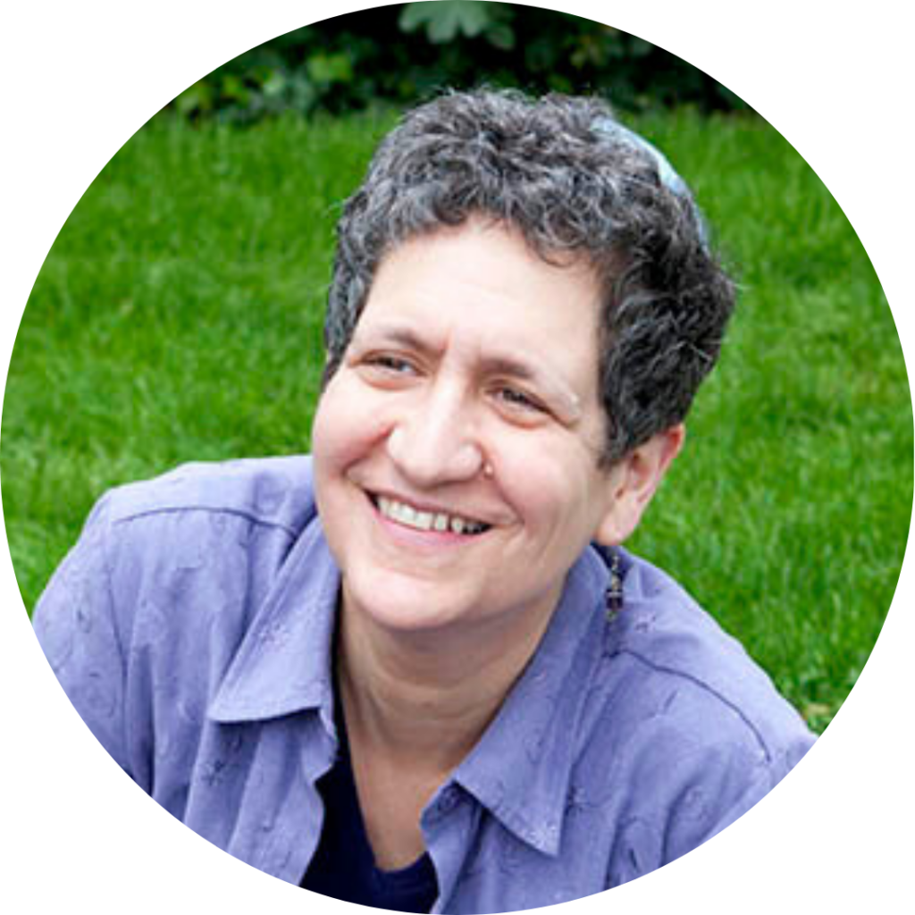 A person with short curly hair and a blue shirt smiling outdoors on grass.