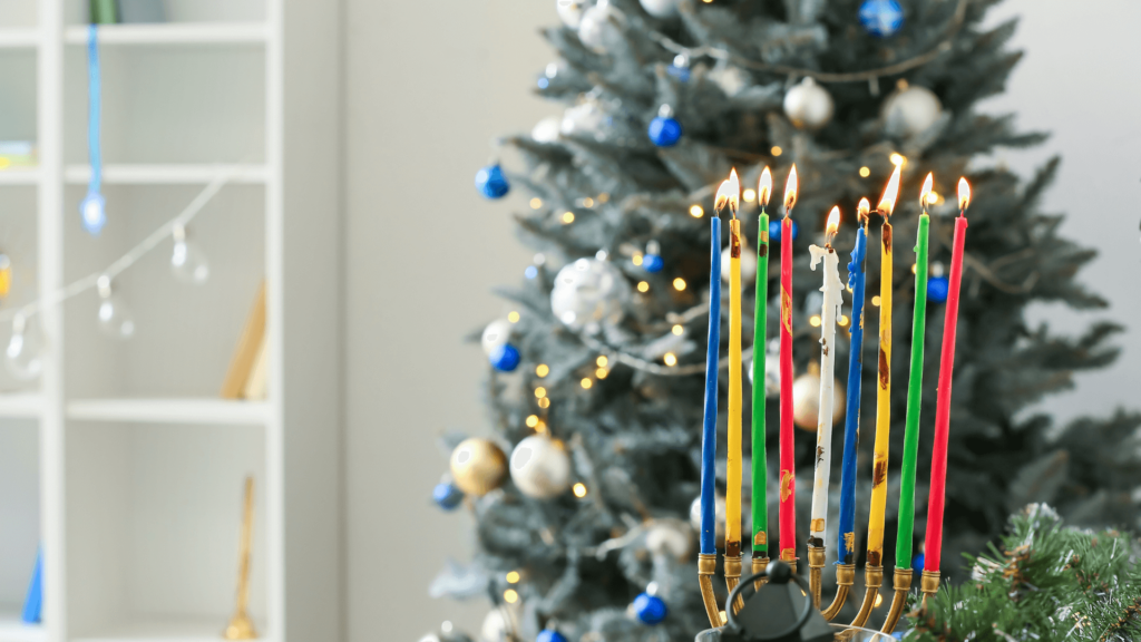 Colorful menorah candles lit in front of a decorated Christmas tree with blue and silver ornaments.