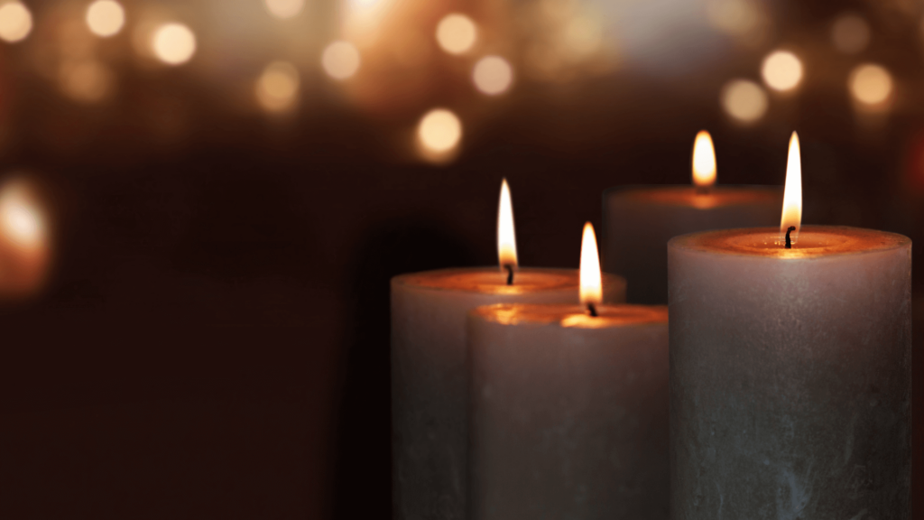 Four lit candles with a blurred background of warm, glowing lights.