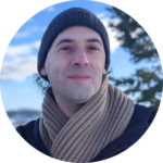 A person wearing a beanie and scarf stands outdoors with a snowy background.