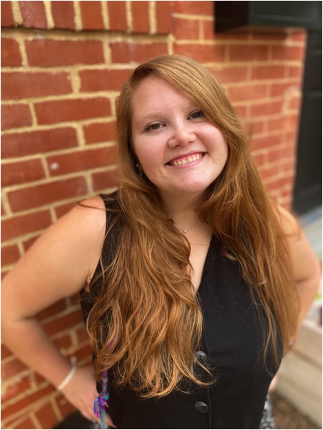 Shira Singelenberg stands in front of a brick wall, wearing a black sleeveless top.