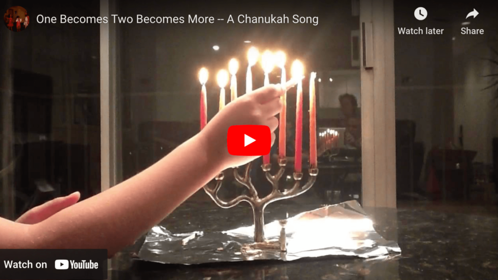 Video still: A hand lighting candles on a menorah, with red and white candles, for a Chanukah celebration.