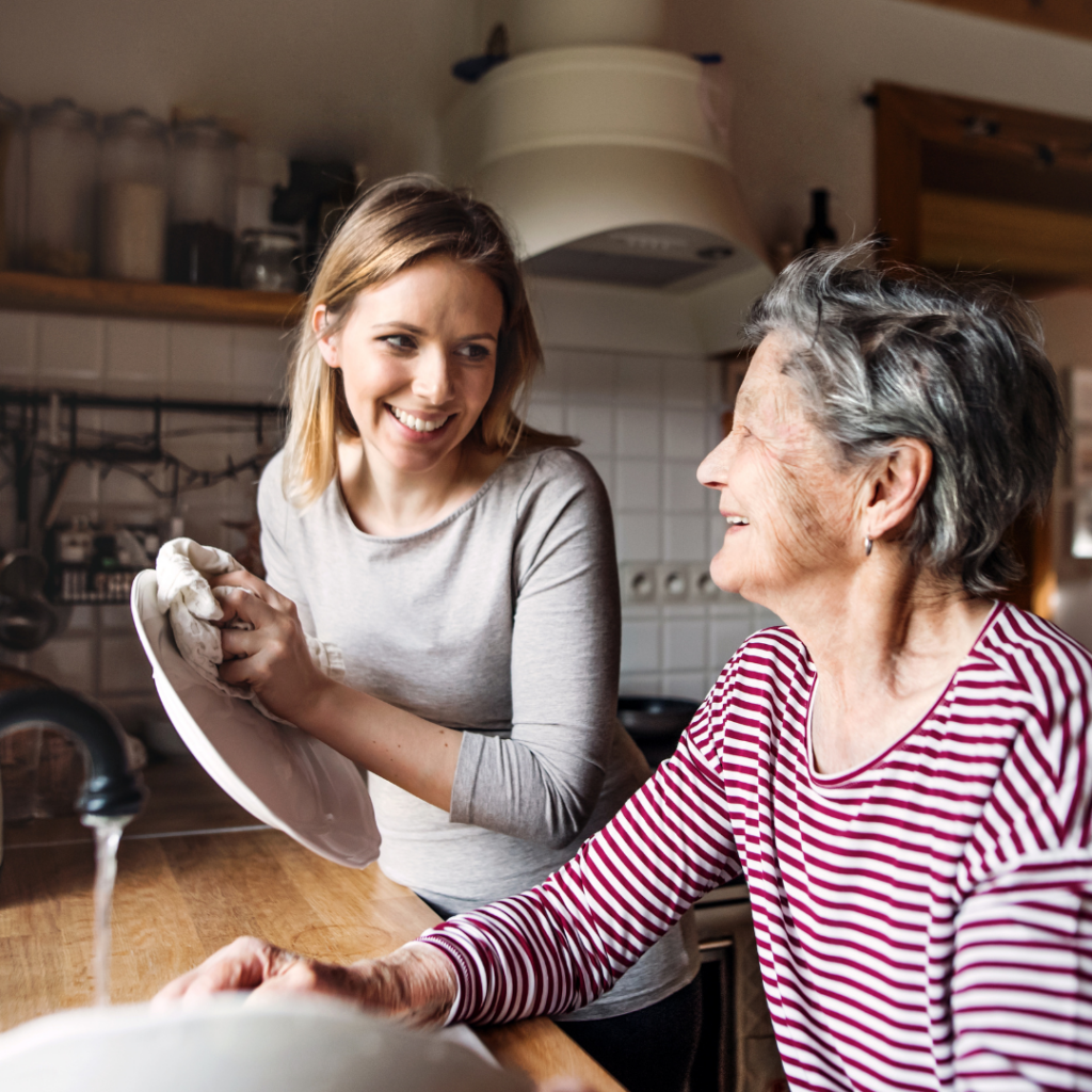 Two women smiling while washing dishes together in a kitchen.