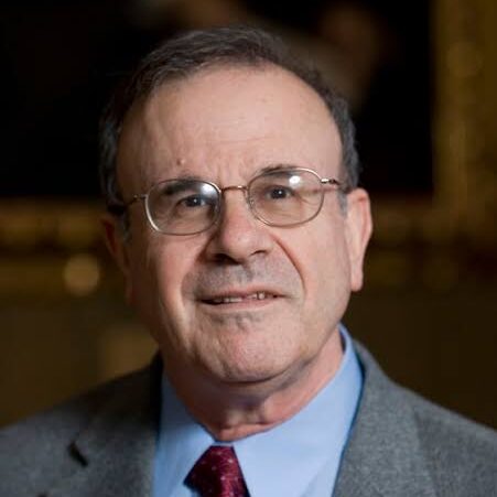 A man in glasses wearing a gray suit jacket, light blue shirt, and red tie.