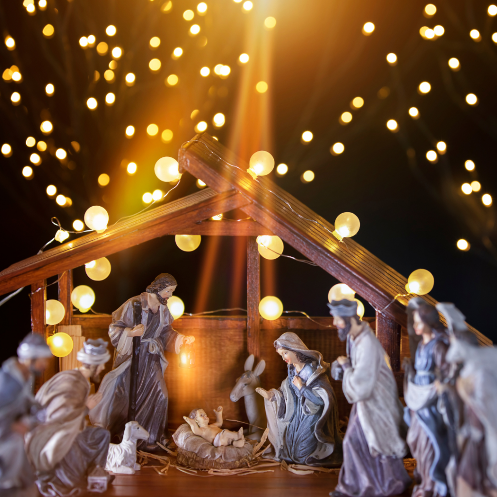 Nativity scene with figurines and warm lighting, surrounded by glowing string lights in the background.