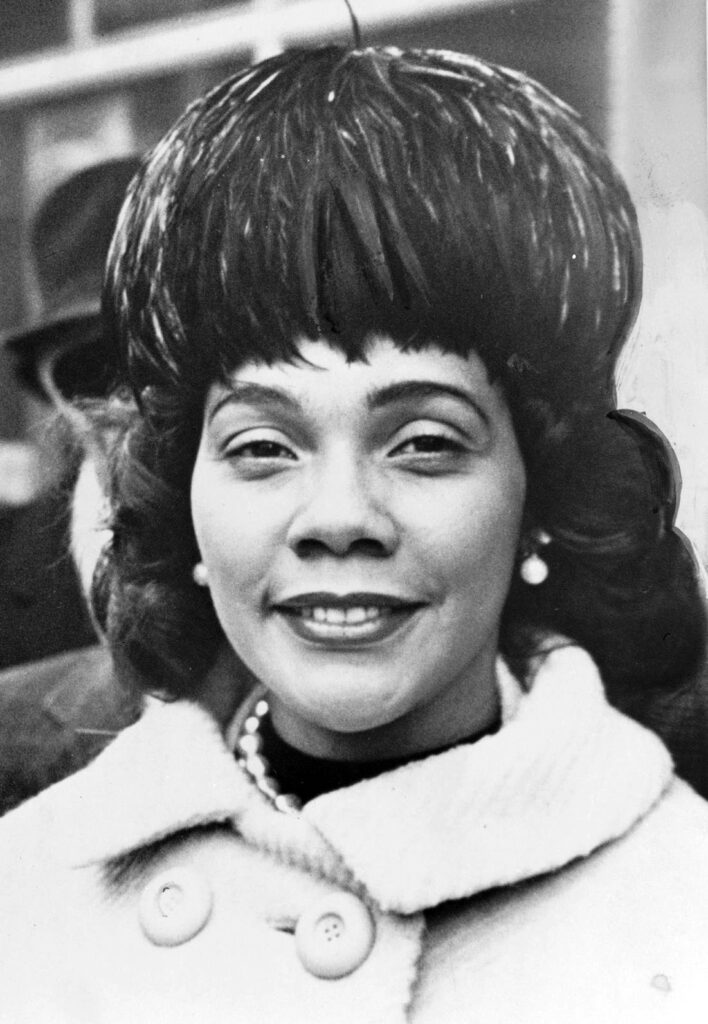 A woman wearing a beret and a coat smiles at the camera in a black and white photo.