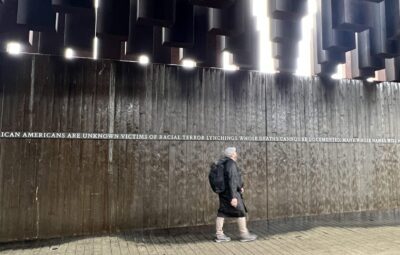 A person walks past a memorial wall with a solemn message about racial terror lynchings.
