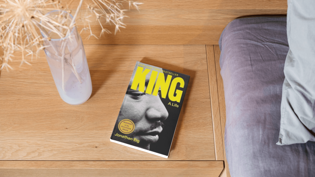 The book King: A Life about Martin Luther King, Jr. on a wooden surface next to a bed with a vase.