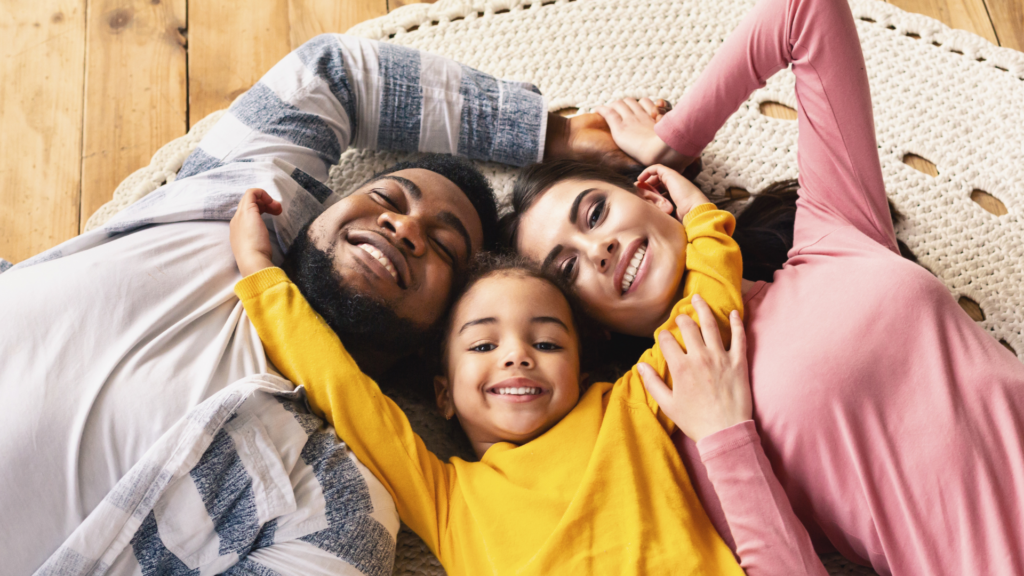 A family of three laying on a rug, smiling and embracing each other.