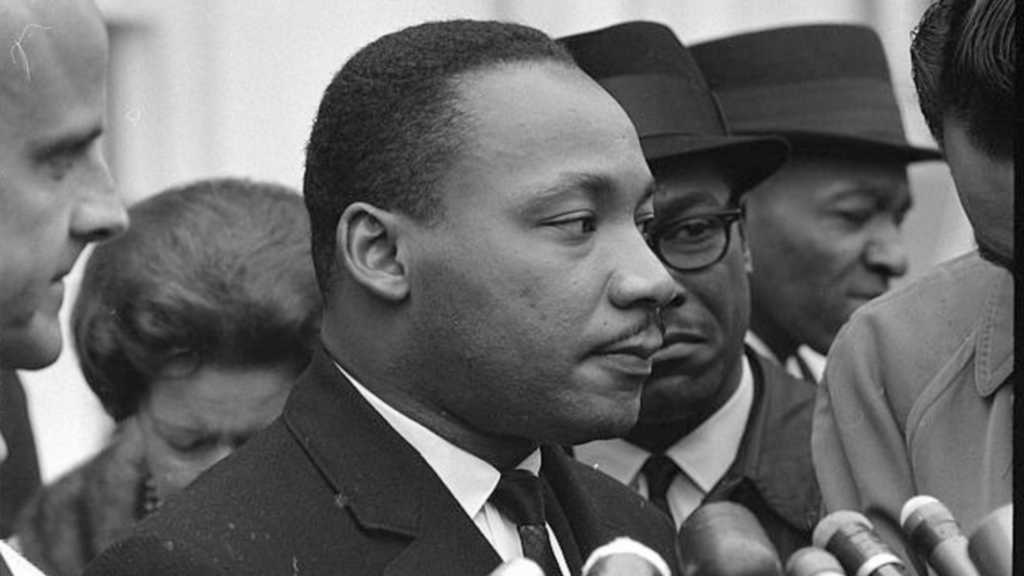 A black and white image of Martin Luther King, Jr. at a public speaking event