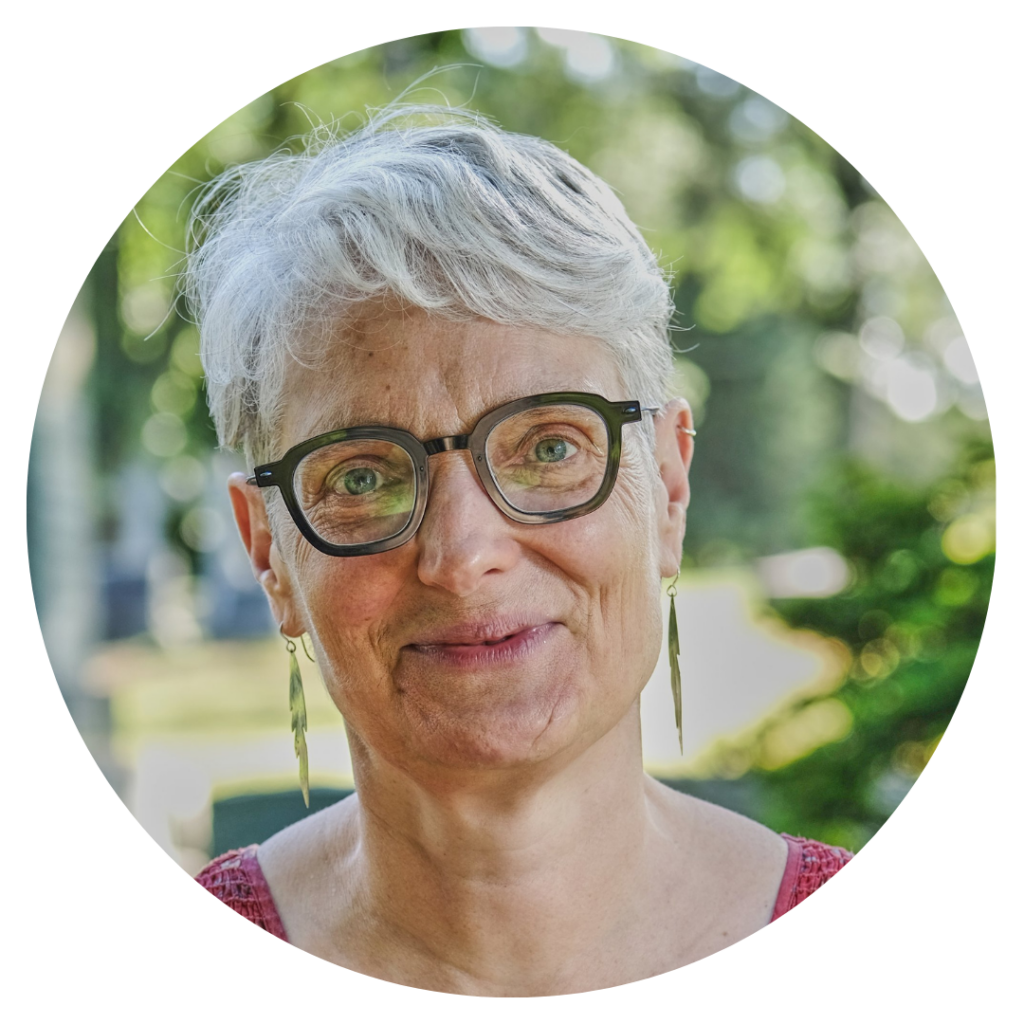 A person with short gray hair and glasses smiling, standing outdoors with trees in the background.